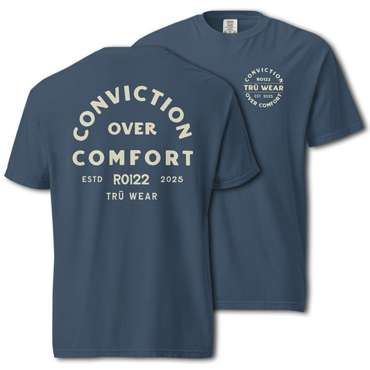 TRŪ Wear Conviction Over Comfort garment-dyed heavyweight tee in Midnight blue, front and back views. Back print reads 'Conviction Over Comfort' in cream arch typography with verse code RO122 and TRŪ Wear below. Front chest features circular badge mark. Comfort Colors 1717 blank. Christian men's Scripture tee.